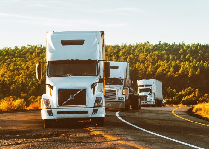 Three semi trucks driving on a highway through a forested landscape in Arizona.